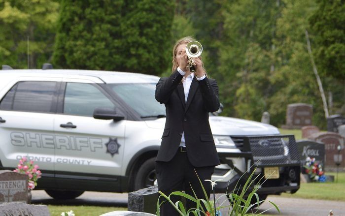 Trumpet player in a suit standing before a sheriff SUV in a grassy outdoor area