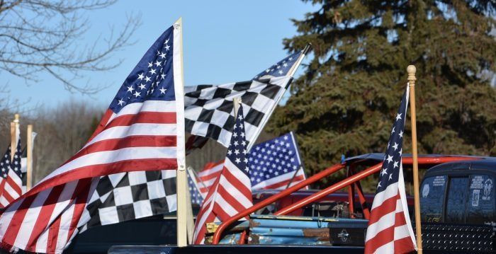 American and checkered racing flags flying beside parked vehicles outdoors