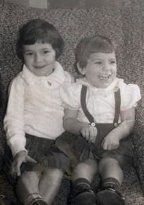 Two children sitting side by side, smiling on a patterned chair.