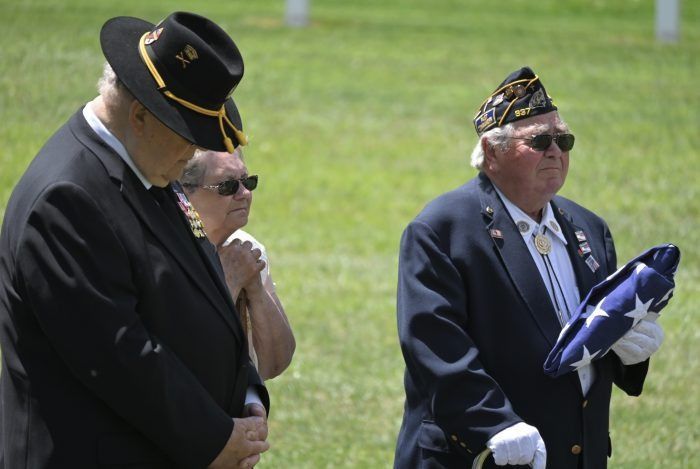 Three veterans in dark uniforms and hats standing outdoors on grass, one holding folded flags.