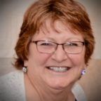 Smiling woman with glasses and short auburn hair against a soft gray background
