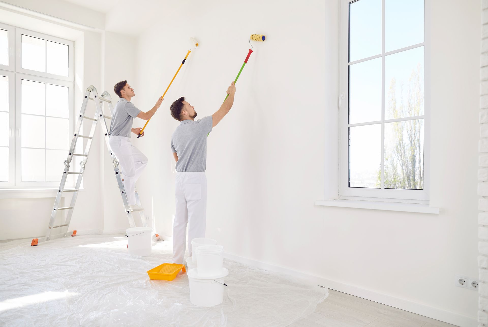 Two men are painting a wall in a room.