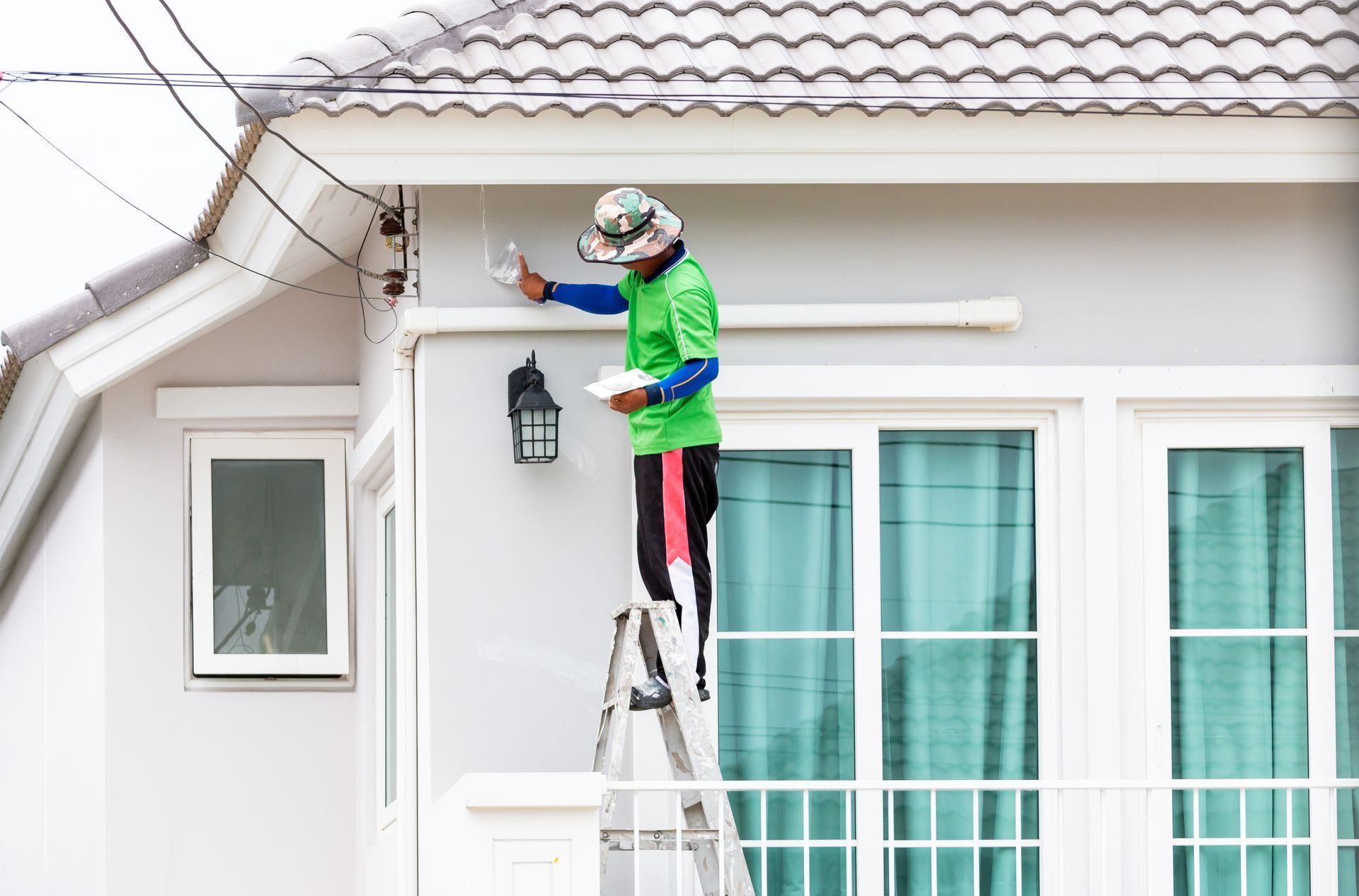 A man is standing on a ladder painting the side of a house.