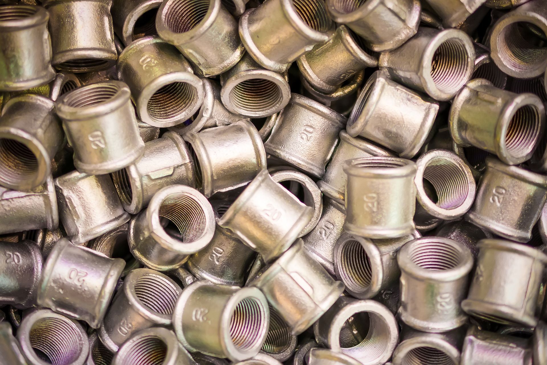 Metal pipe fittings, piled together, showing internal threads.
