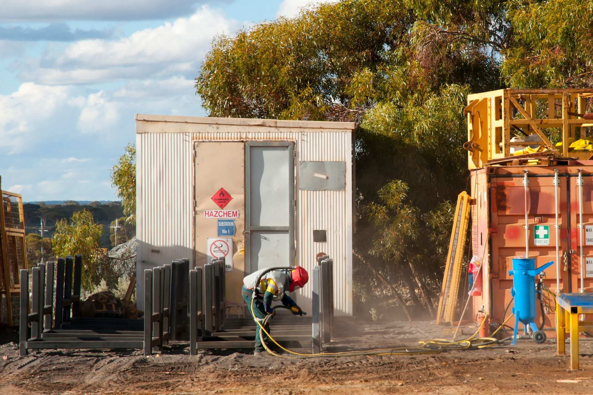Person in protective suit working near a small building with hazardous materials signage, next to containers.