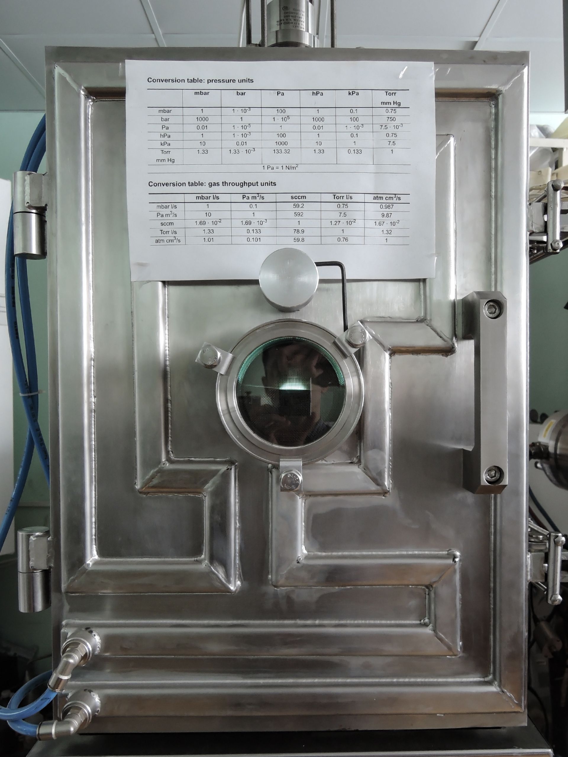 Stainless steel vacuum chamber with a circular window and attached document.