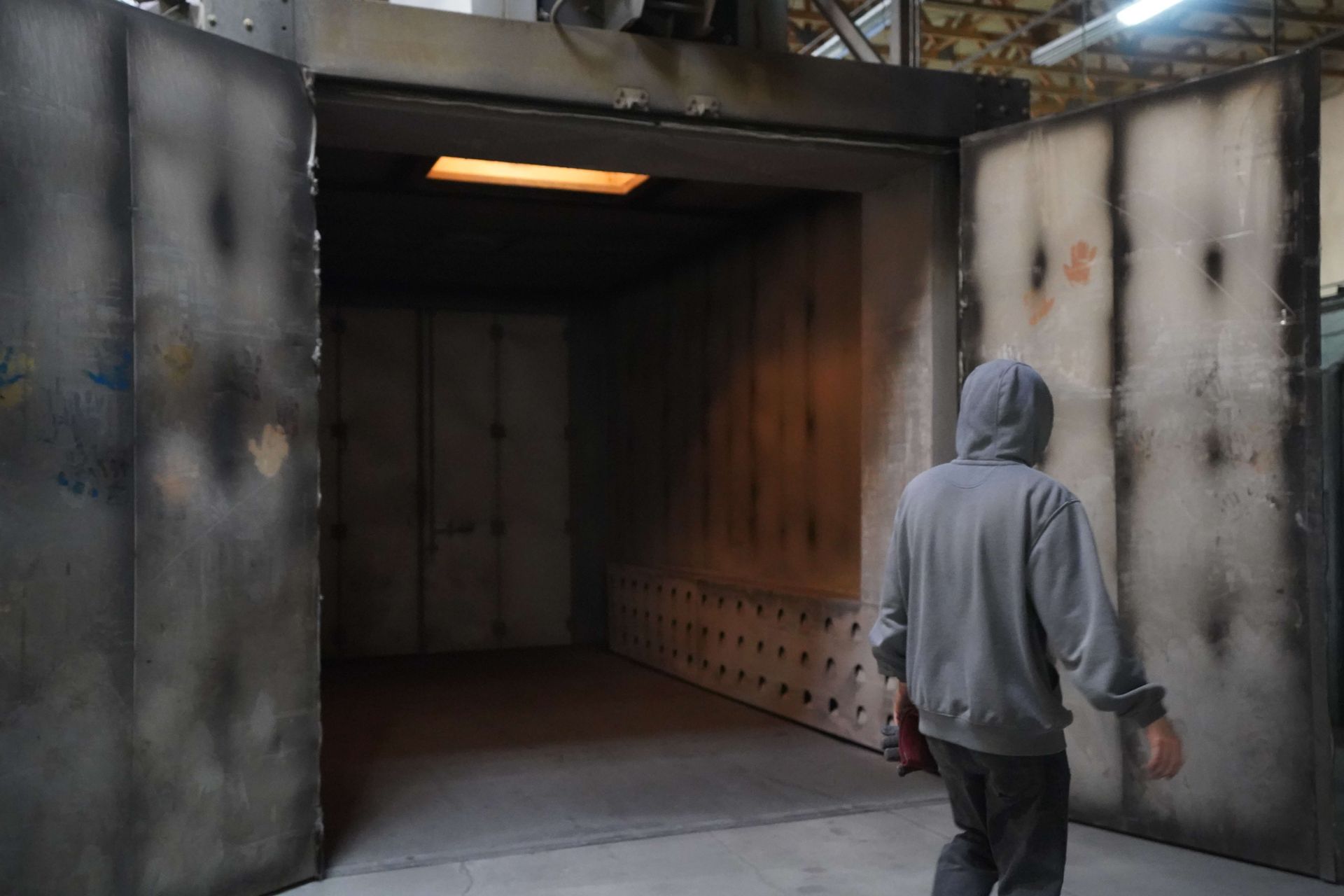 Person in a gray hoodie walking toward a large industrial doorway with open metal doors.