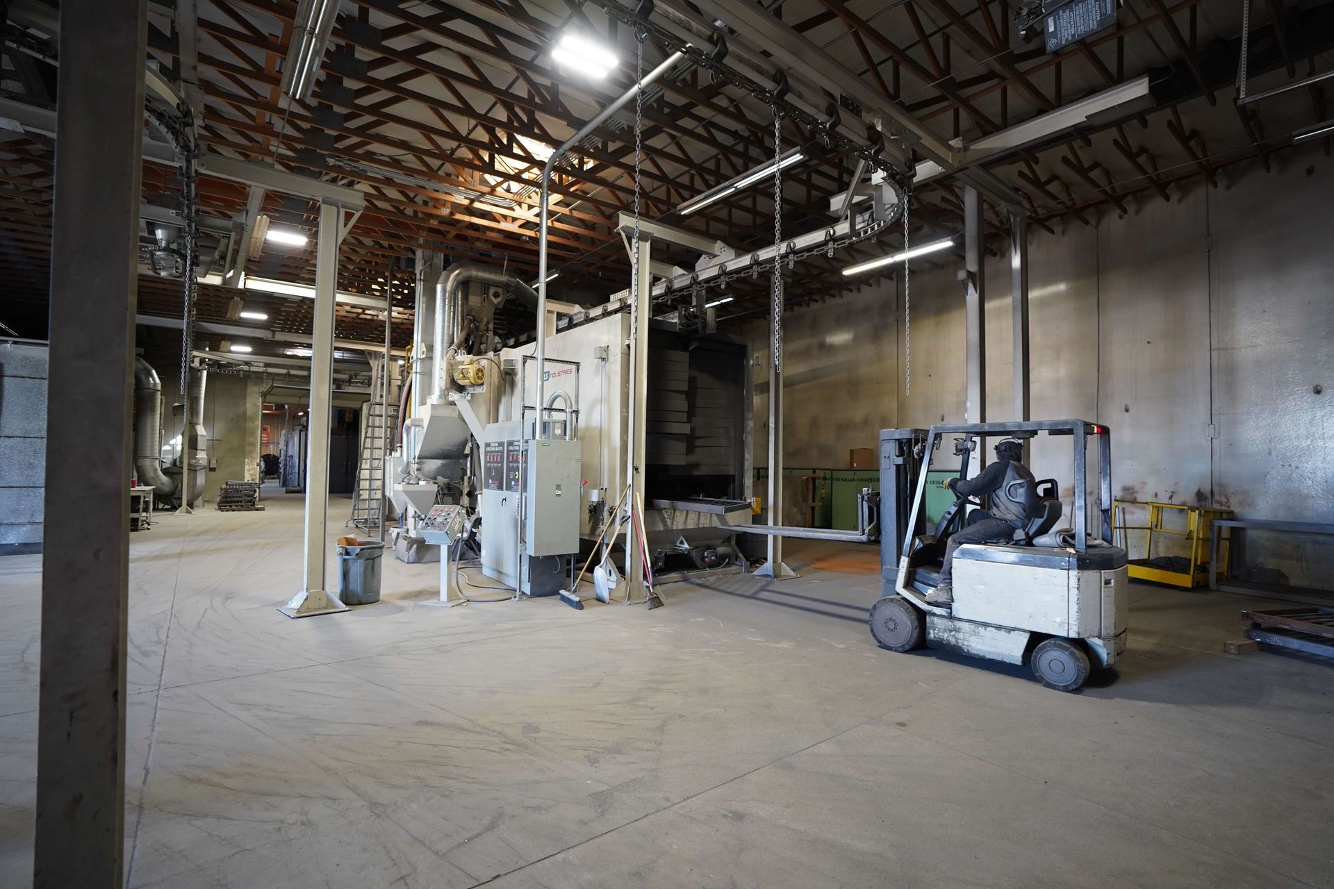 Warehouse interior with machinery, forklift, and a person driving it.