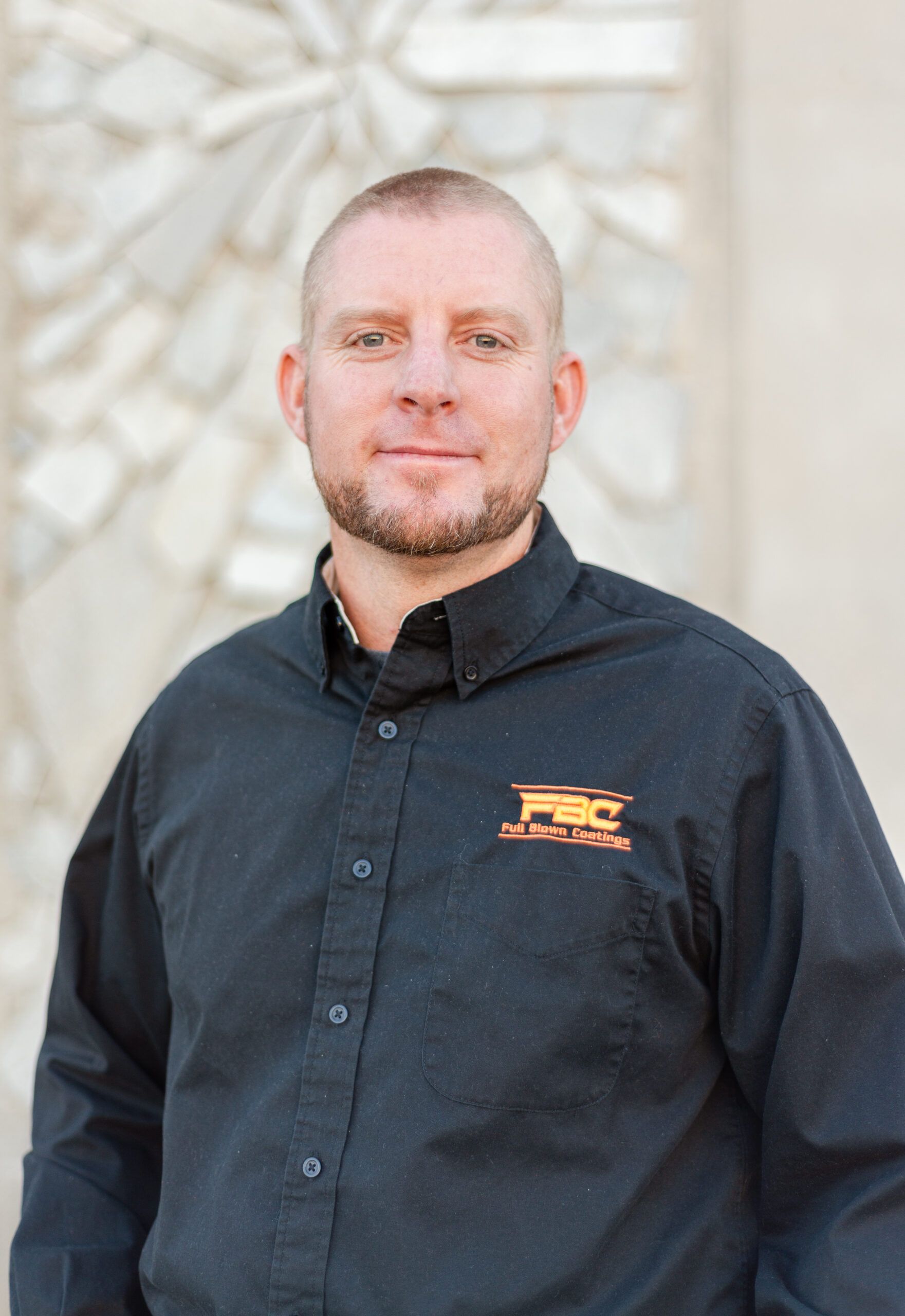 A man in a black shirt is standing in front of a stone wall.