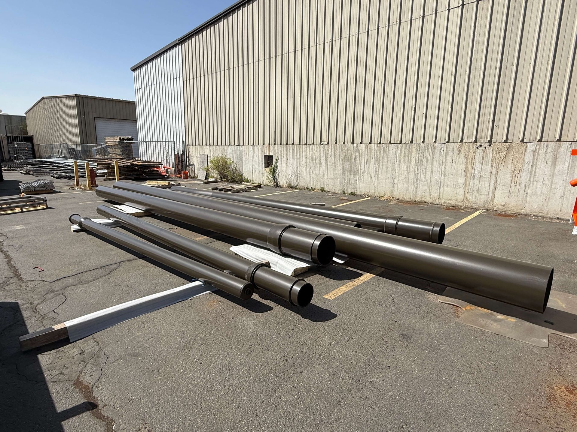 A bunch of sand blasted powder coated pipes are stacked on top of each other in a parking lot in front of a building.