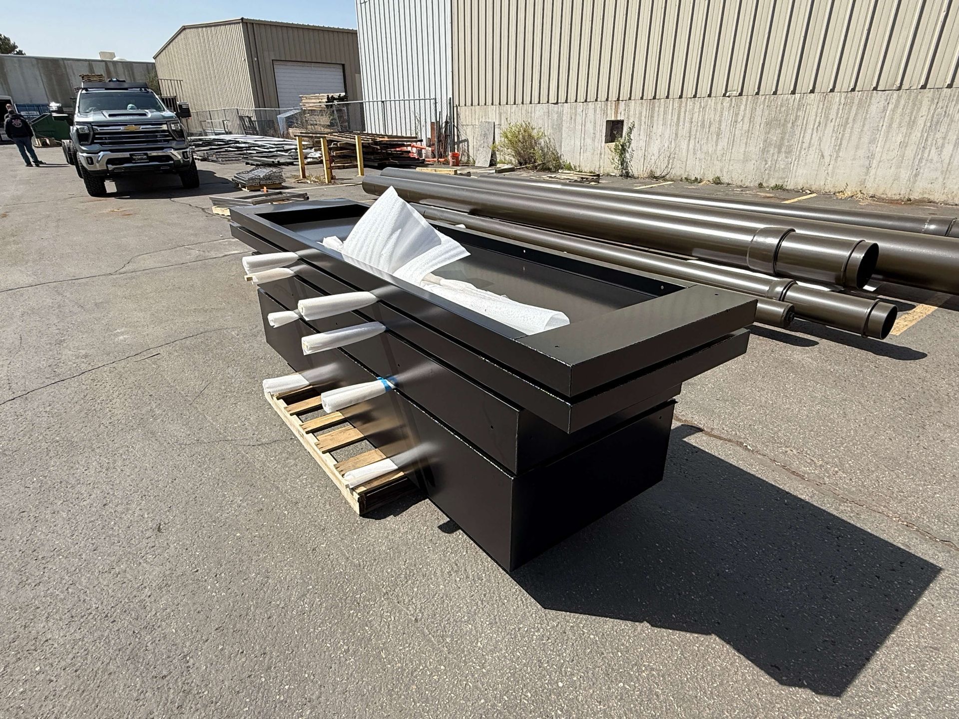 A large piece of powder coated metal is sitting on top of a wooden pallet in a parking lot.