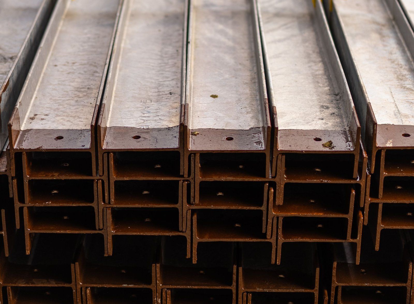 Stacked structural steel I-beams with mill scale and light surface rust in a warehouse