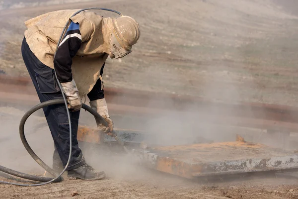 A man is sandblasting a piece of metal with a hose.