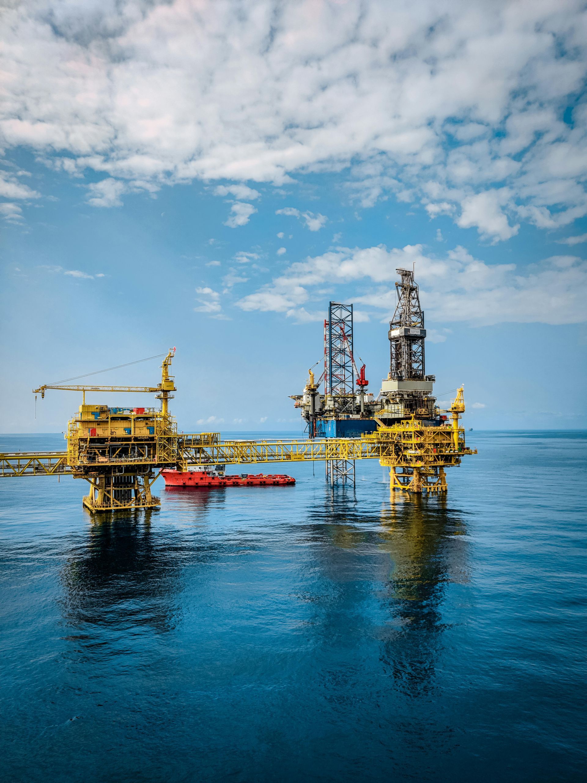 Offshore oil platform with yellow and red structures on calm blue sea under a cloudy sky