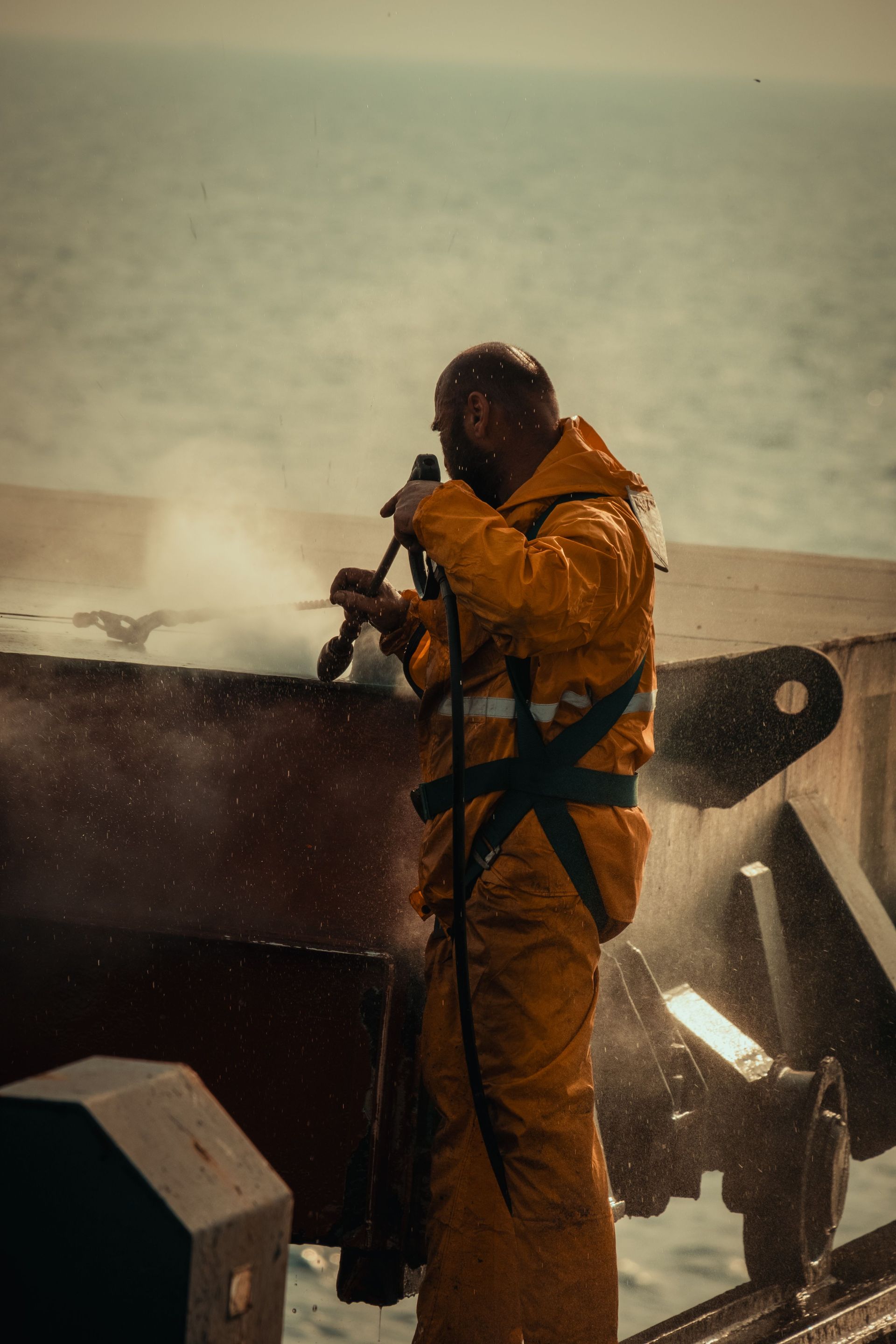 Firefighter in yellow gear dousing a smoking vehicle by the water.