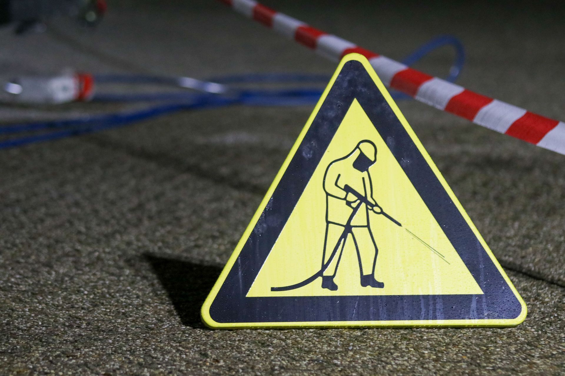 Yellow caution sign showing a worker digging on a road at night with cones and tape in the background