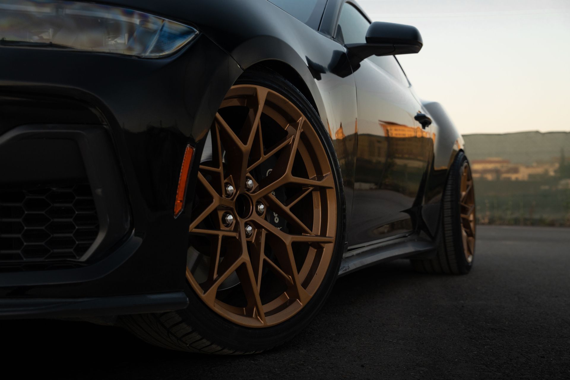 Black sports car with bronze color wheels parked on a road at sunset