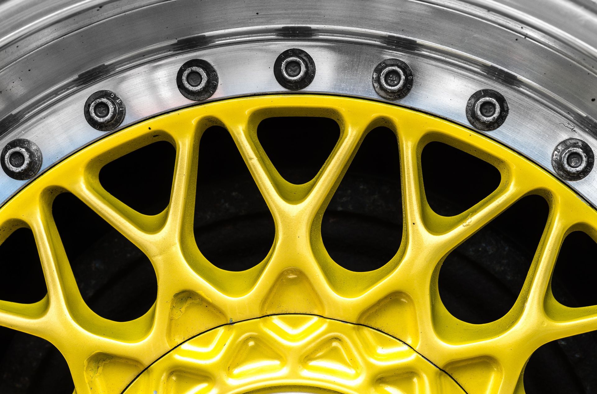 Close-up of a yellow alloy wheel rim with black bolts and silver metal trim