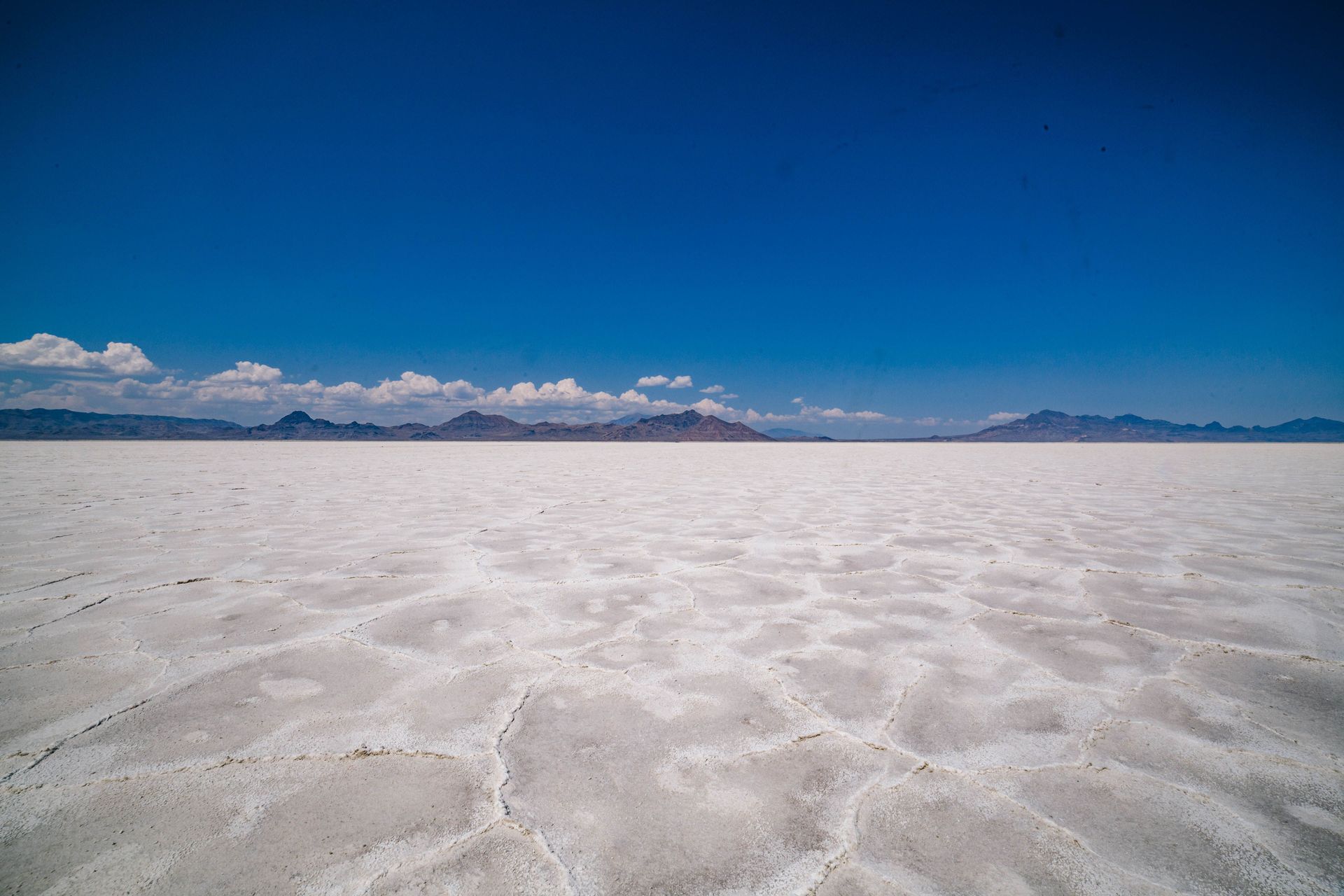 Expansive white salt flat under a deep blue sky with distant mountains on the horizon