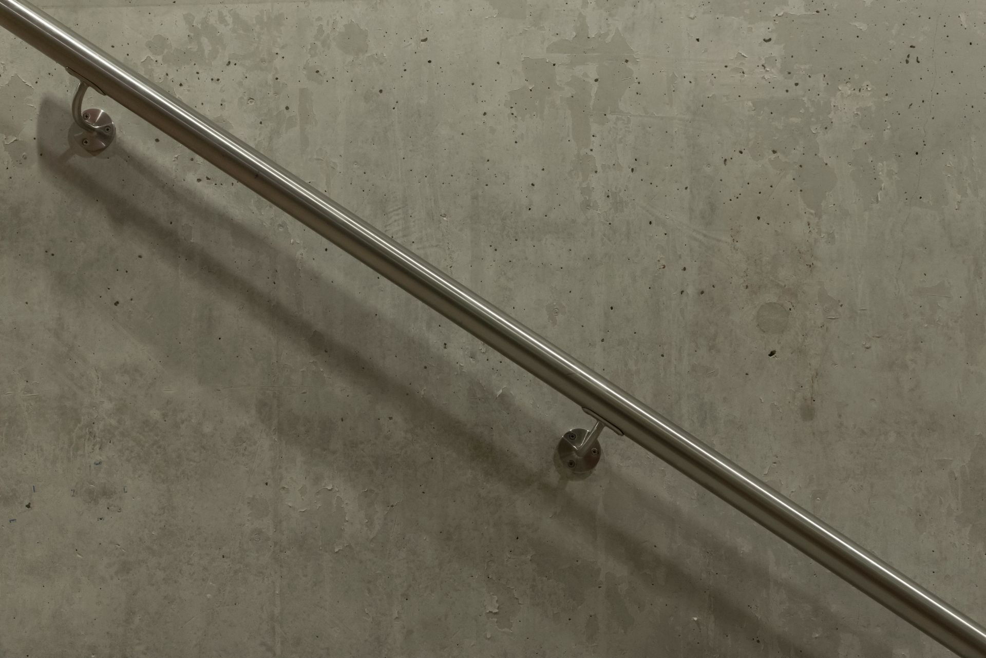 Brushed stainless steel handrail mounted on a concrete wall with soft shadows