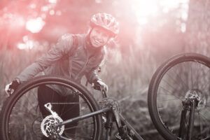 A woman cyclist repairs her mountain bike in a forest at dawn.