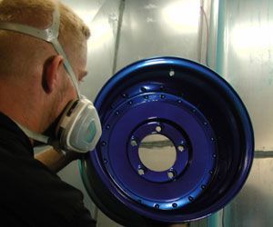 A man wearing a mask is painting a blue wheel.