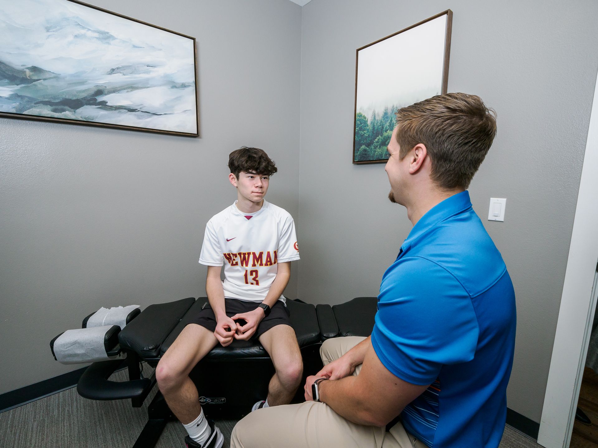 A man is talking to a young boy who is sitting on an adjustment table.