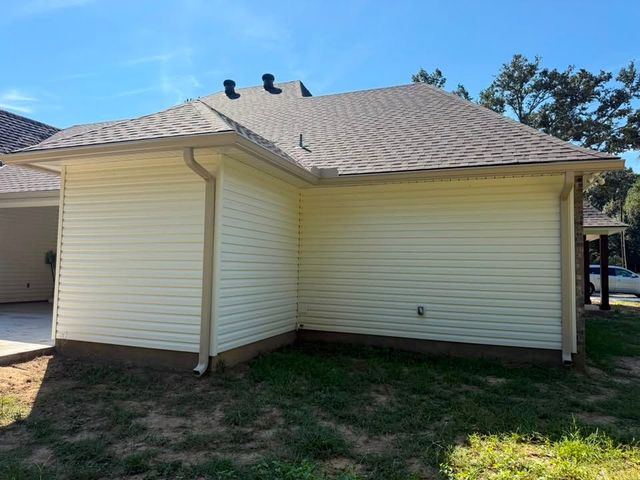 Back of a beige house with light roof, small covered patio, and grassy yard