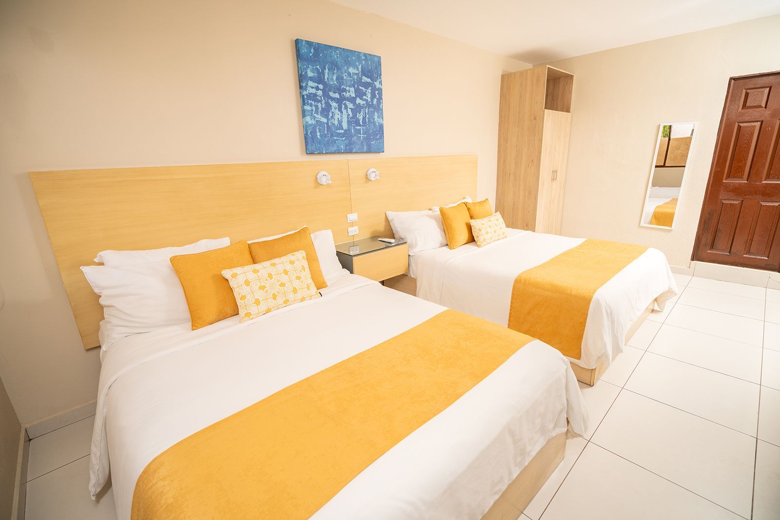 A hotel room with two beds featuring white linens, yellow runners, and matching yellow accent pillows.