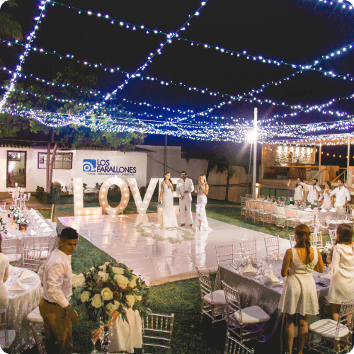 Outdoor evening wedding reception with a bride and groom on a dance floor by large illuminated