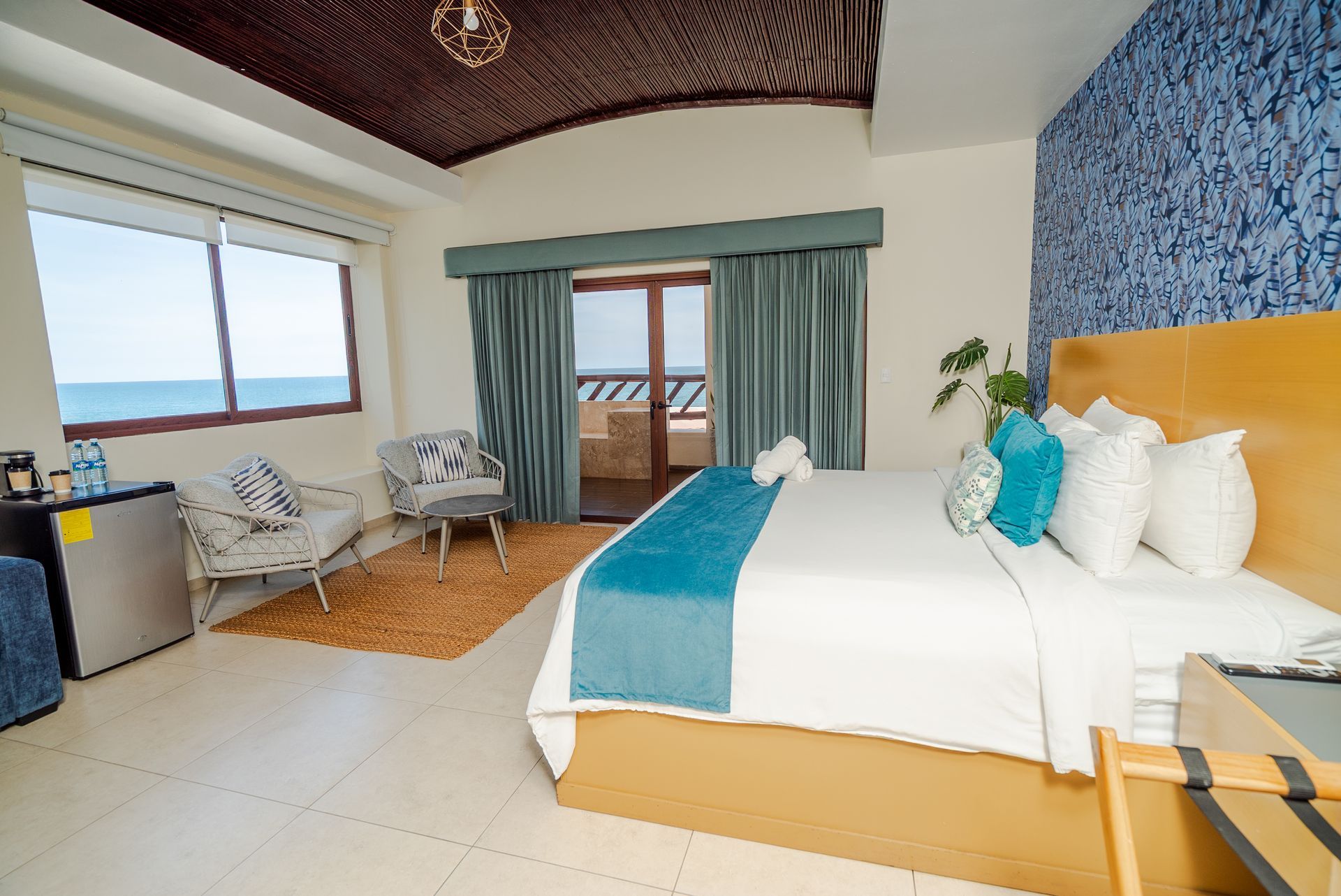 Bright hotel room with ocean view, king bed, blue accents, balcony, and seating area