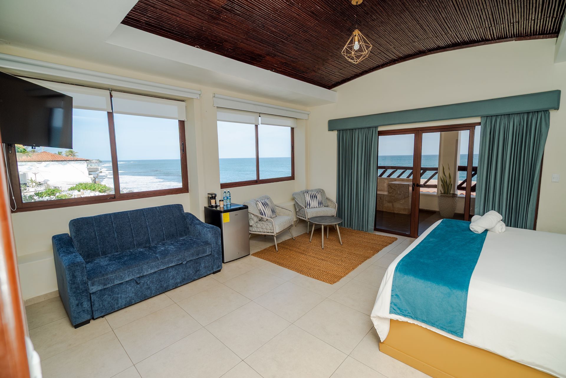 Bright hotel room with blue couch, bed, large windows, and ocean view