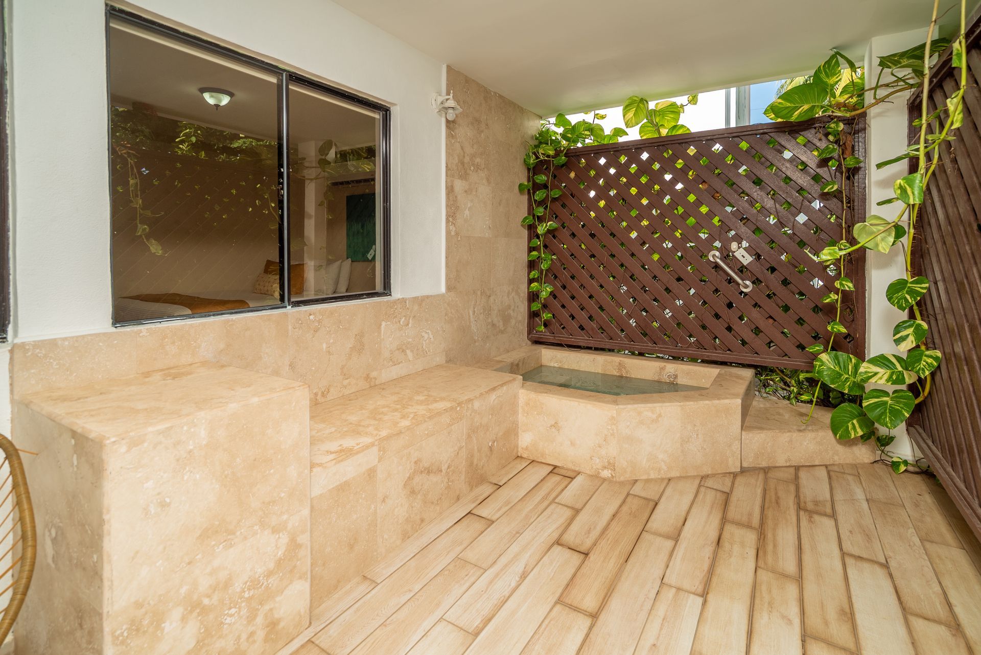 Stone patio seating area with bench, tiled floor, lattice privacy screen, and green vines
