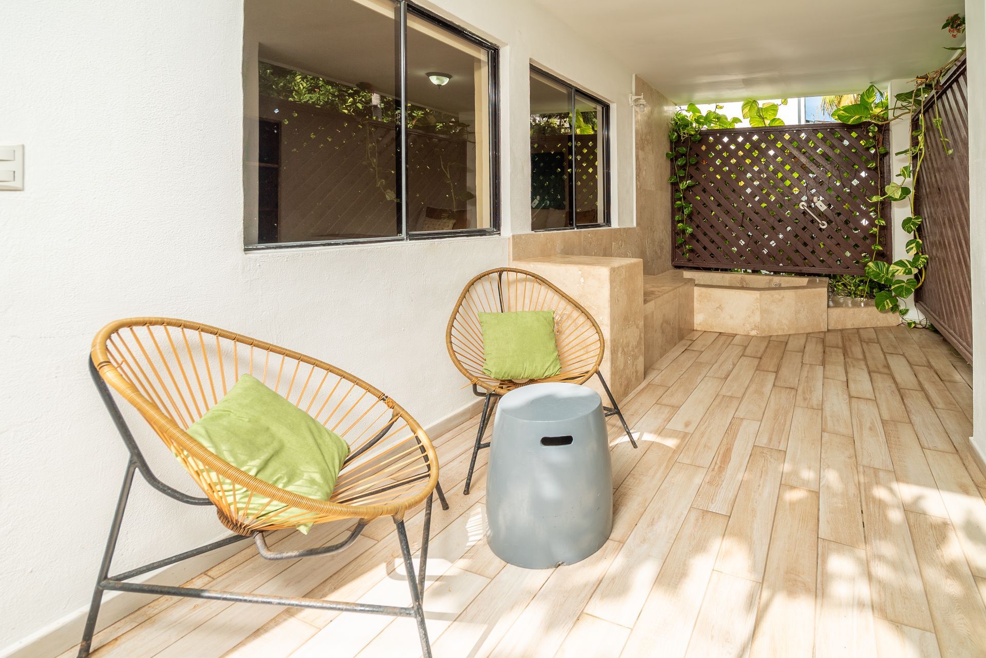 Covered patio with wicker chairs, green cushions, wood deck, and lattice privacy screen