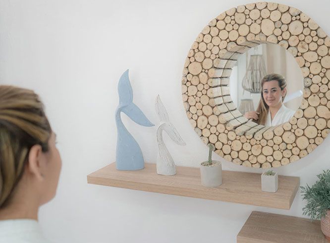 A person views their reflection in a round wood-slice mirror above a shelf with two whale-tail sculptures.