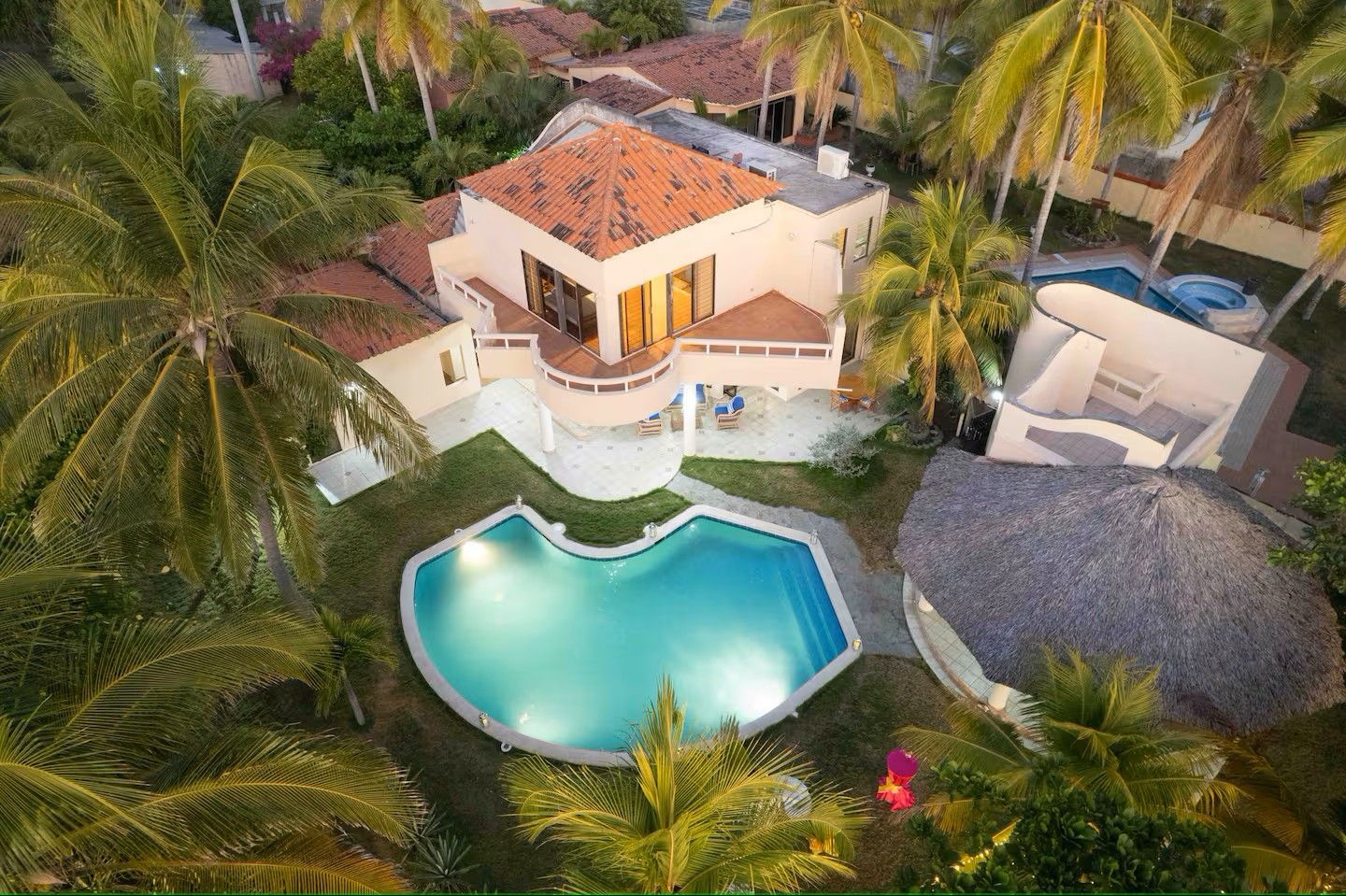 Aerial view of a tropical villa with a turquoise pool surrounded by palm trees.