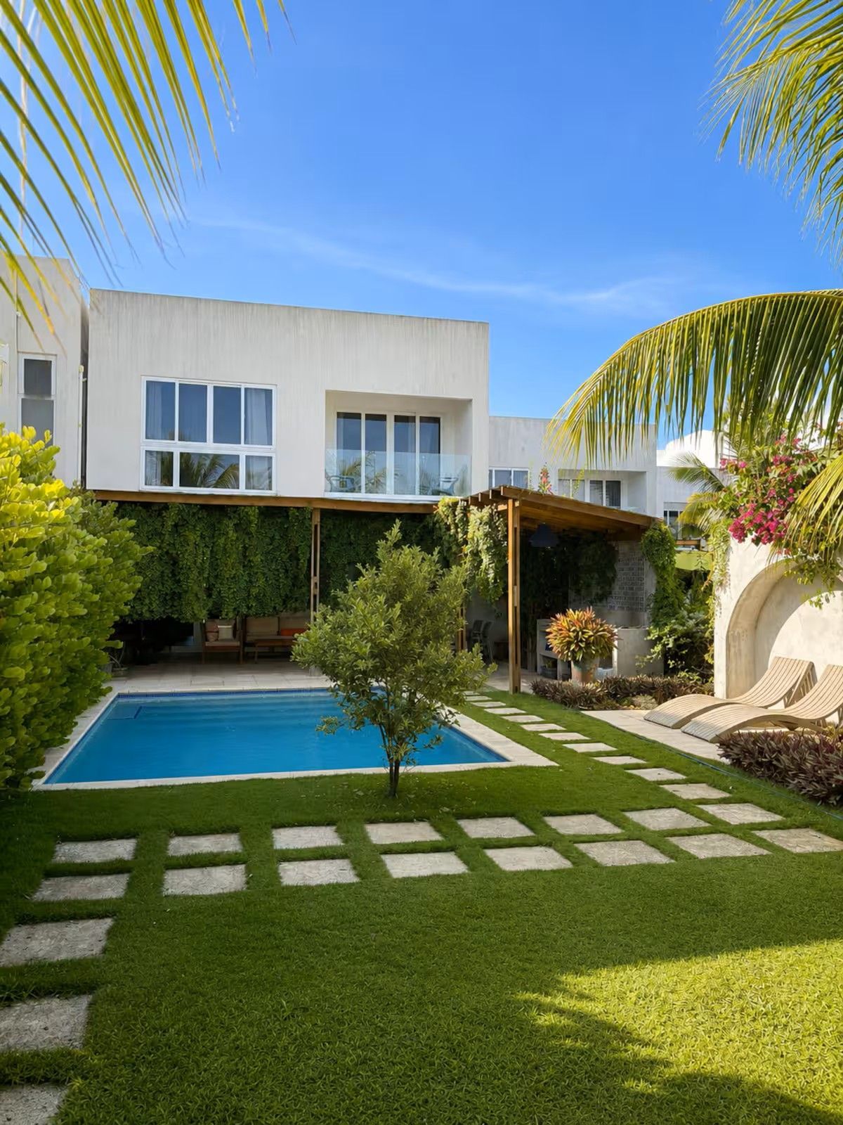 Modern home courtyard with a small pool, green lawn, stepping stones, and palm trees