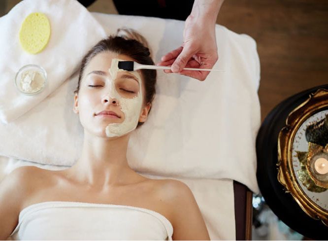 A professional applies a facial mask to a relaxed person lying on a spa treatment table.