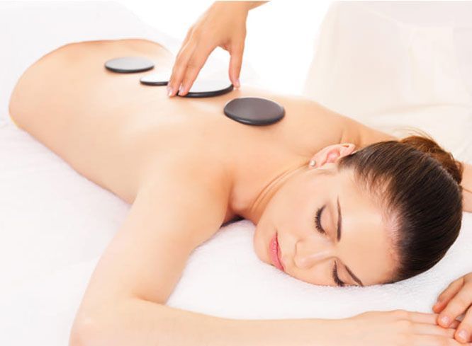 A person lies on a massage table while receiving hot stone therapy, with smooth dark stones placed along their back.