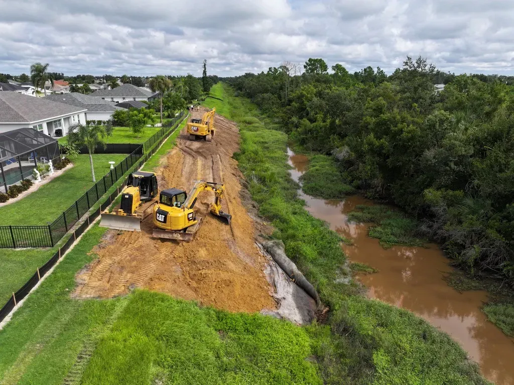 DeSoto ditch drainage project: excavator and dump truck working along the waterway behind homes