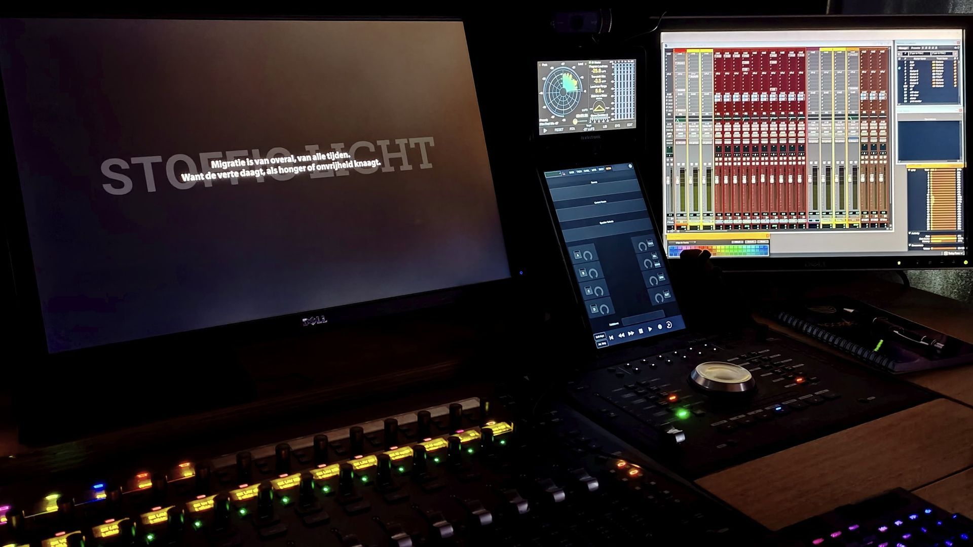 Een professionele lichtregelconsole met verlichte knoppen, meerdere monitoren en software-interfaces in een donkere ruimte.