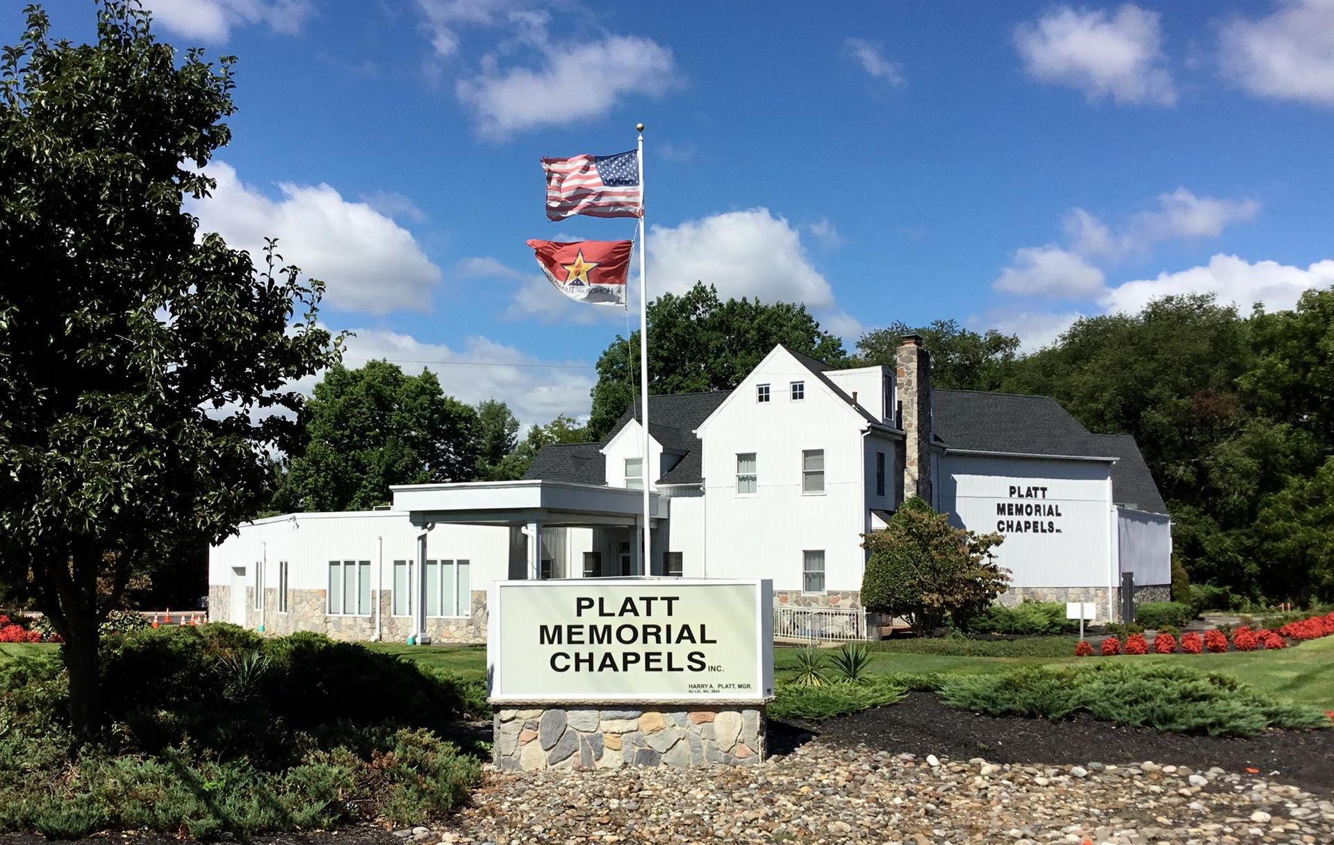 Platt Memorial Chapel with U.S. flag, white building, and landscaped flower beds under a blue sky