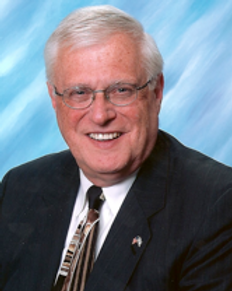 Studio portrait of a smiling man in a dark suit and tie against a blue backdrop