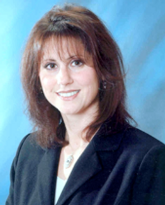 Smiling woman in a black blazer against a blue studio backdrop