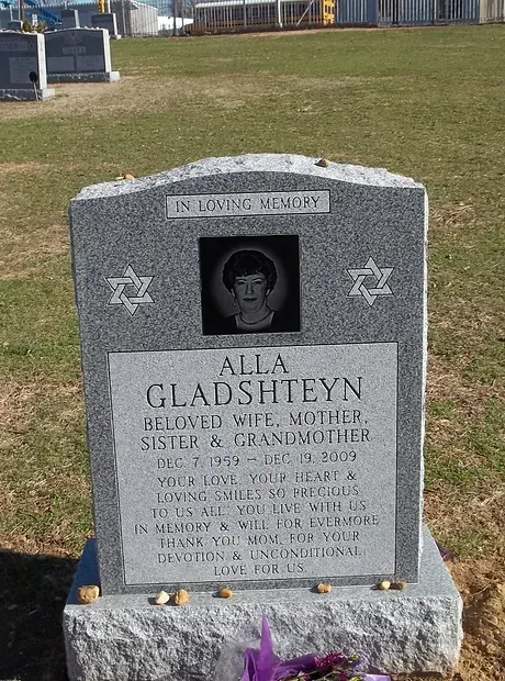 Gray gravestone with engraved portrait in a grassy cemetery, marked for Alla Glashteyn.