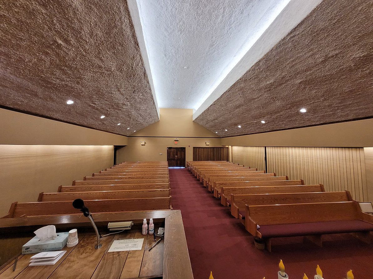 Empty church pews with red carpet aisle and wooden ceiling, viewed from the pulpit.