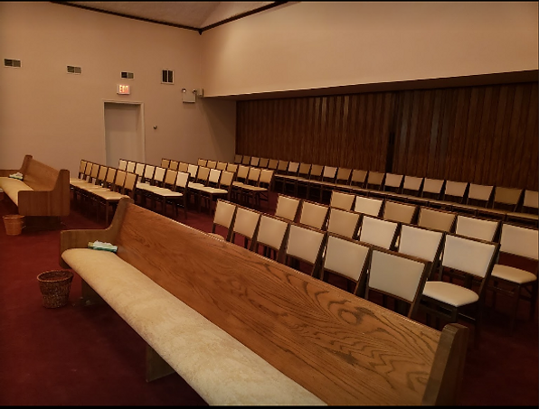 Empty courtroom gallery with rows of beige folding chairs and wooden benches