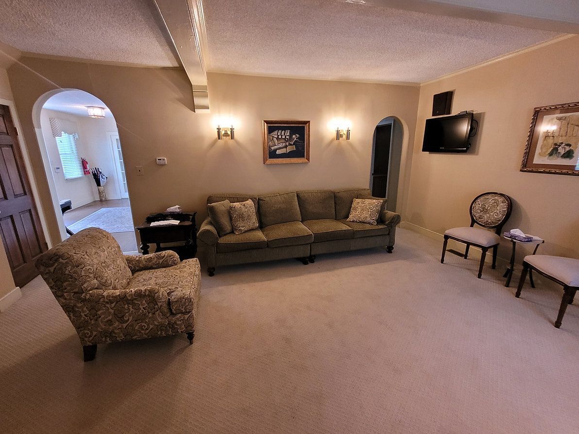 Spacious beige living room with sofa, armchair, wall art, and arched doorway to adjacent room.