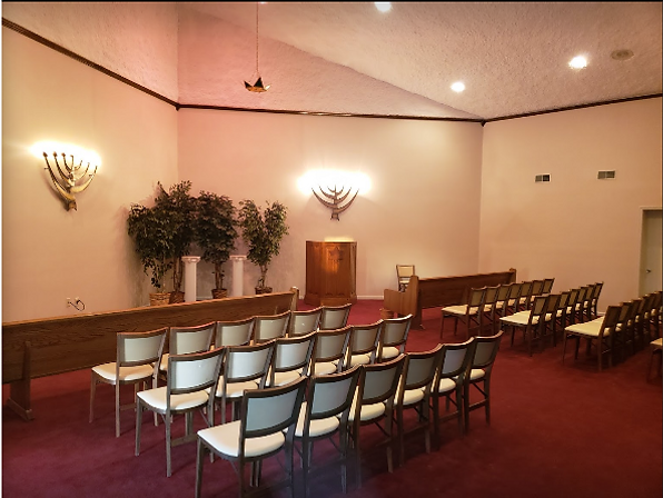 Empty chapel or meeting room with rows of chairs, podium, and wall sconces on red carpet