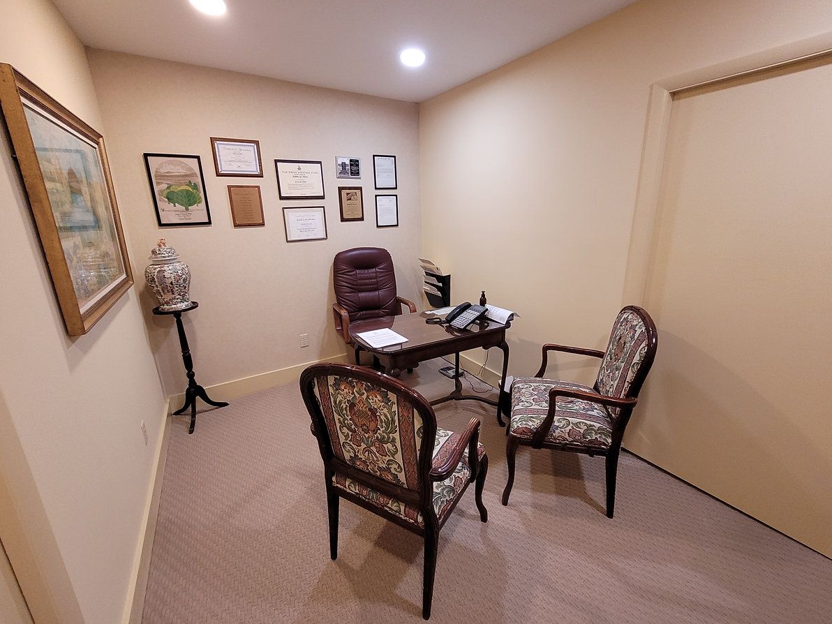 Small waiting room with two chairs, a table, wall art, and a small desk against beige walls.
